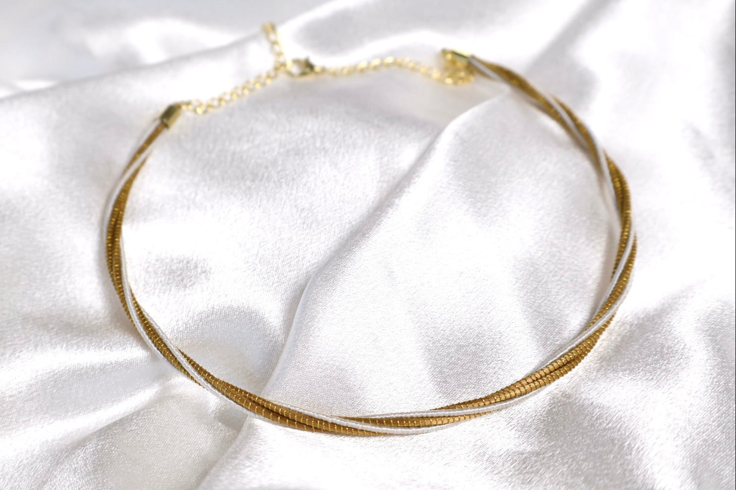 close up of golden grass twisted choker intertwined with white thread AquaBrasil